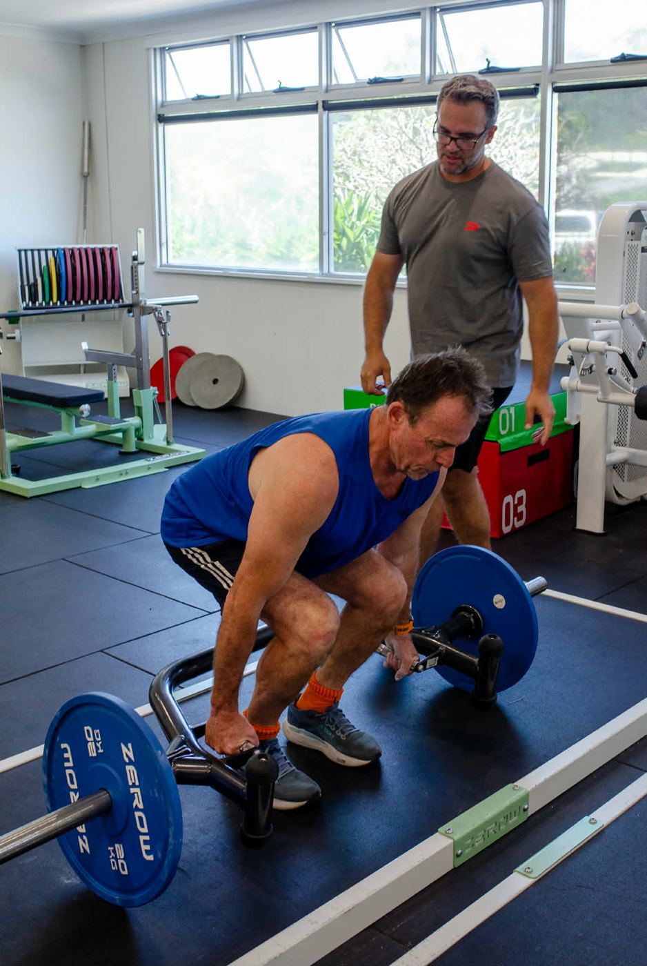 Client preparing to lift a trap bar while Mathew watches